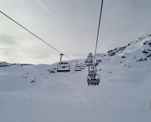 Skiers riding a chairlift at Lac des Vaux in Verbier on the first weekend of the 2025/26 winter season, surrounded by fresh early snow.