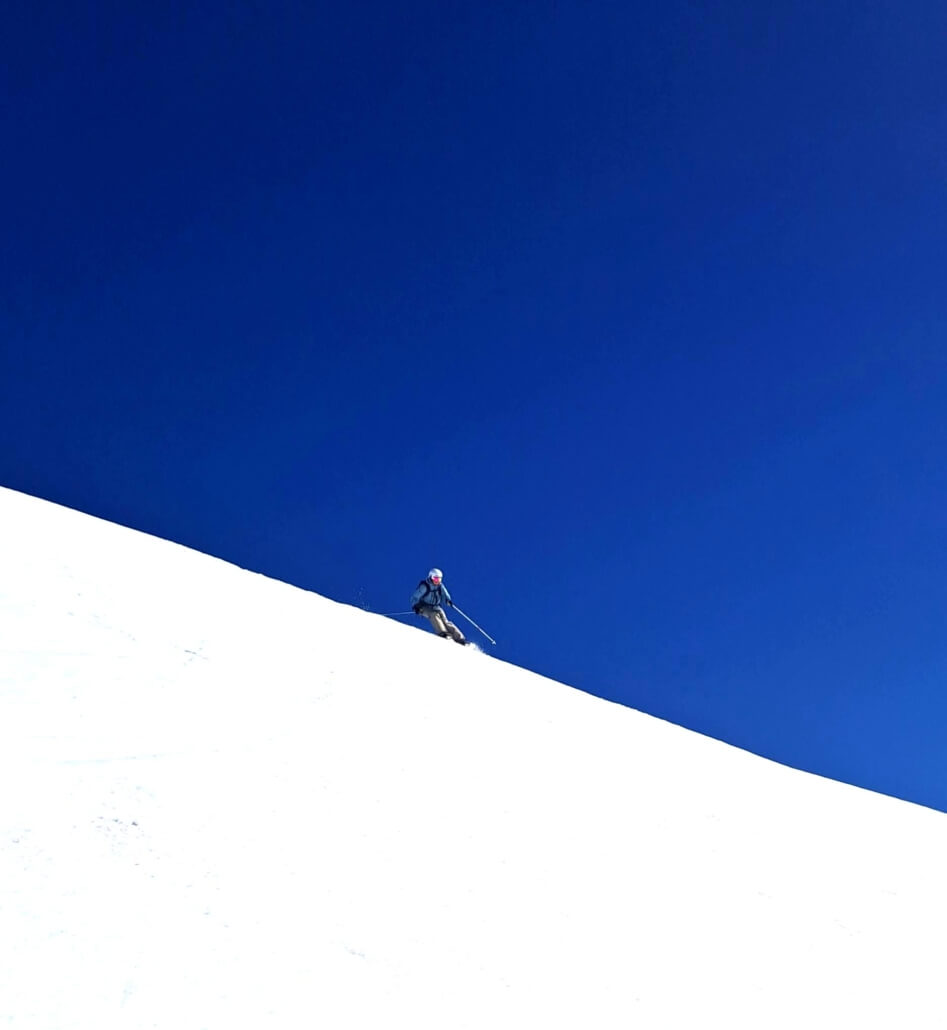 Client skiing off piste in Verbier on bright white snow under clear blue sky