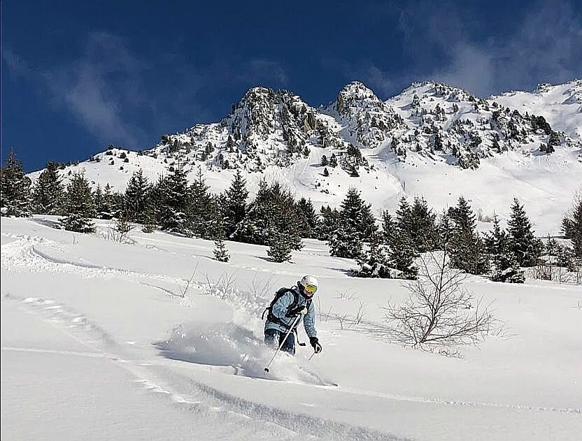 Emma skiing through fresh powder beneath dramatic snow-covered mountain peaks in the Swiss Alps.